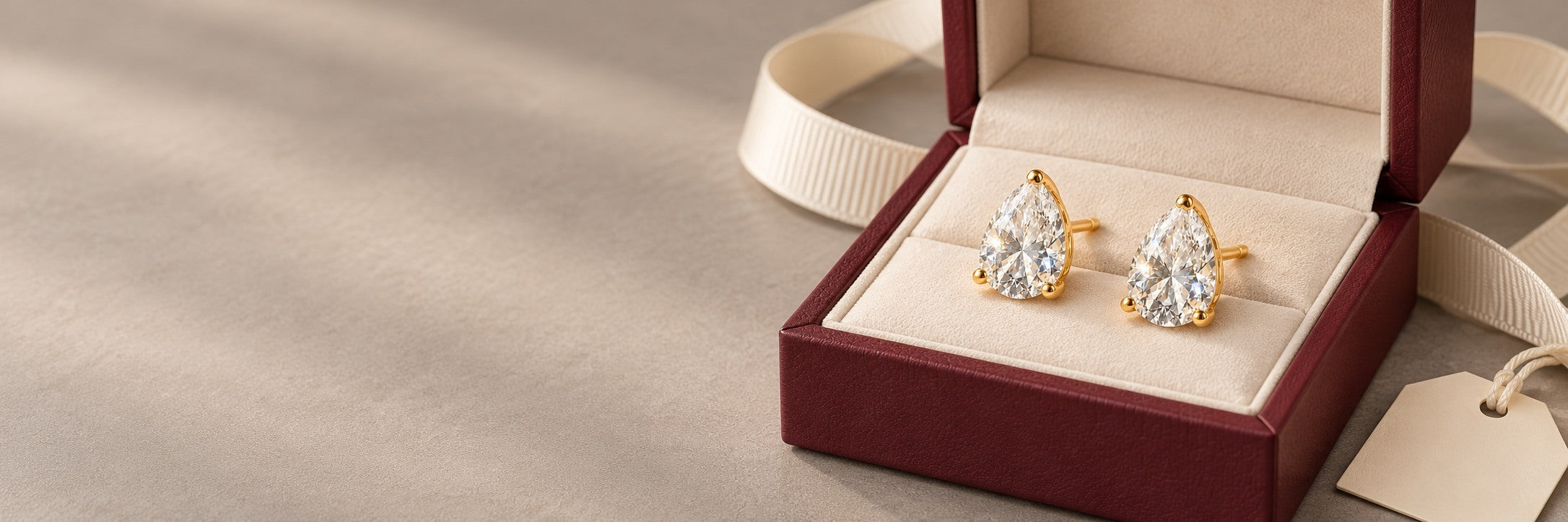 Pear-cut gold stud earrings displayed in a burgundy gift box